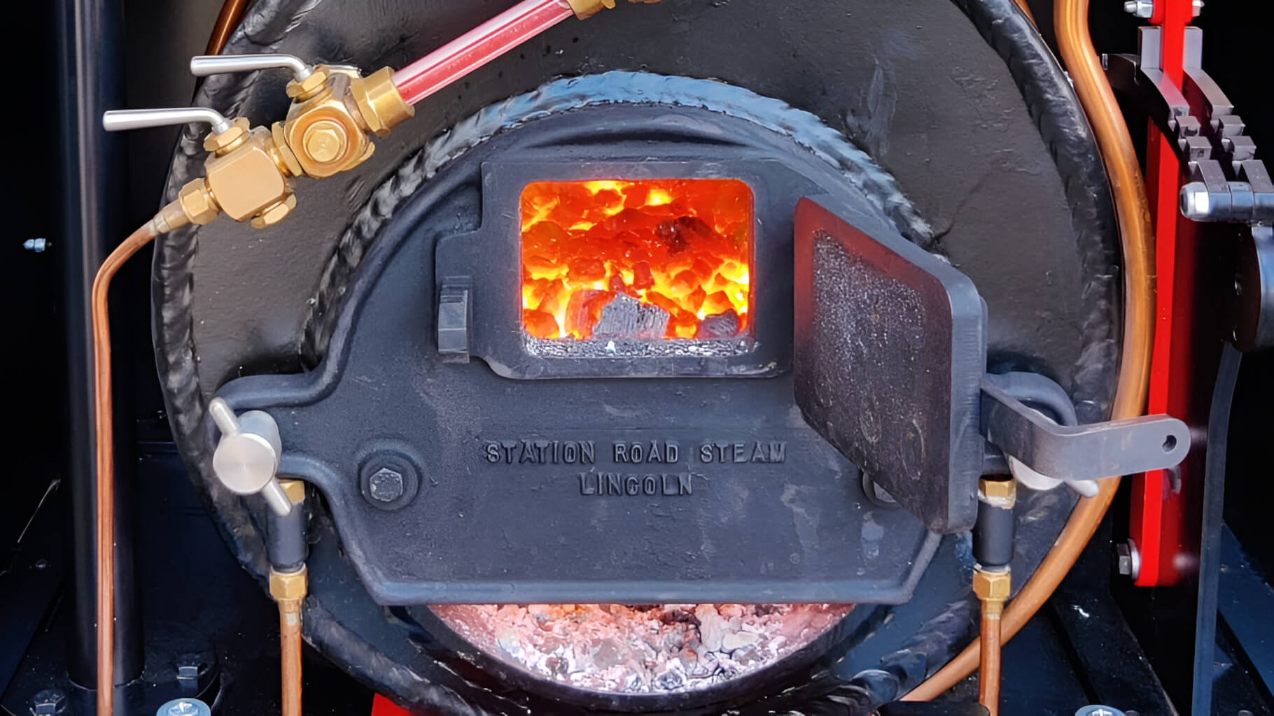 Open firebox of a Station Road Steam miniature locomotive with glowing coals.